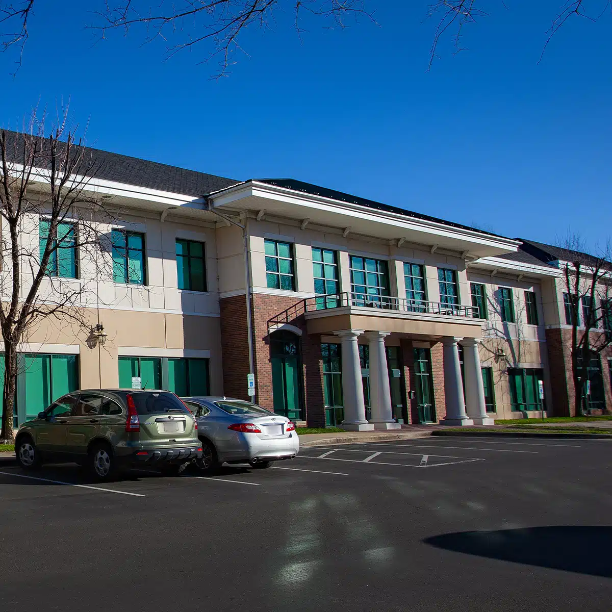 Exterior view of a two-story building with a brick and tan facade, green-tinted windows, and a portico with four columns....