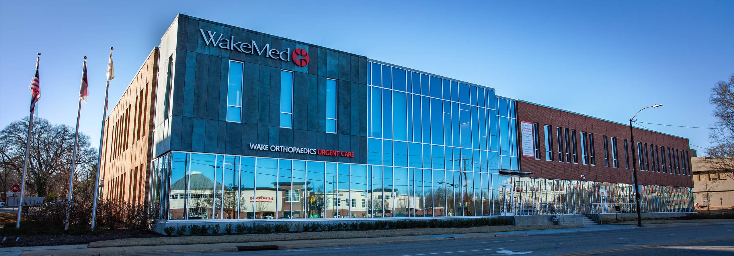 WakeMed building with glass and brick facade, "Wake Orthopaedics Urgent Care" on the front, under a clear blue sky.