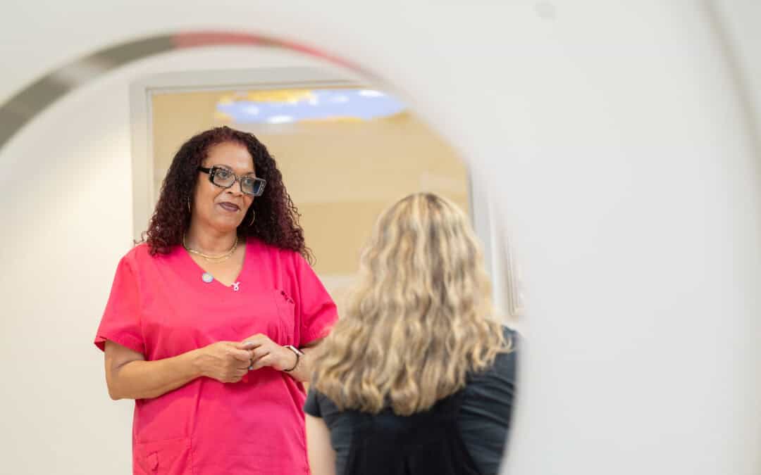 Female medical professional in pink scrubs talking to a female patient with blonde hair.